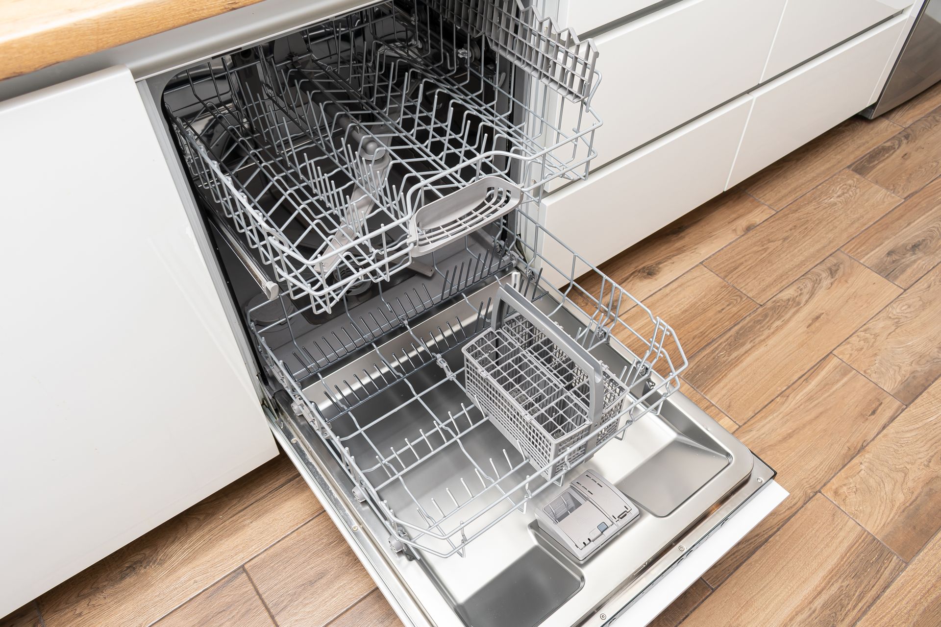 Open dishwasher with empty racks, showing top and bottom levels, set in a light kitchen. Open dishwasher with empty racks, showing top and bottom levels, set in a light kitchen.