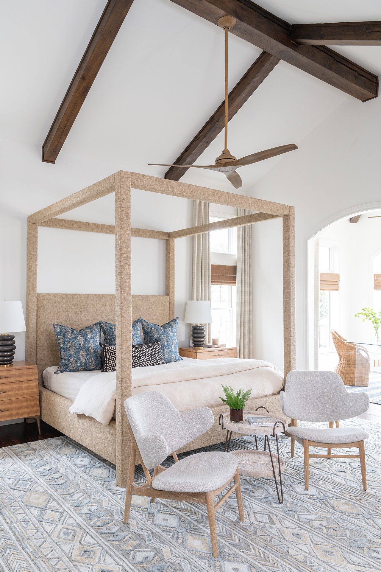 A bedroom with a canopy bed , chairs and a ceiling fan.