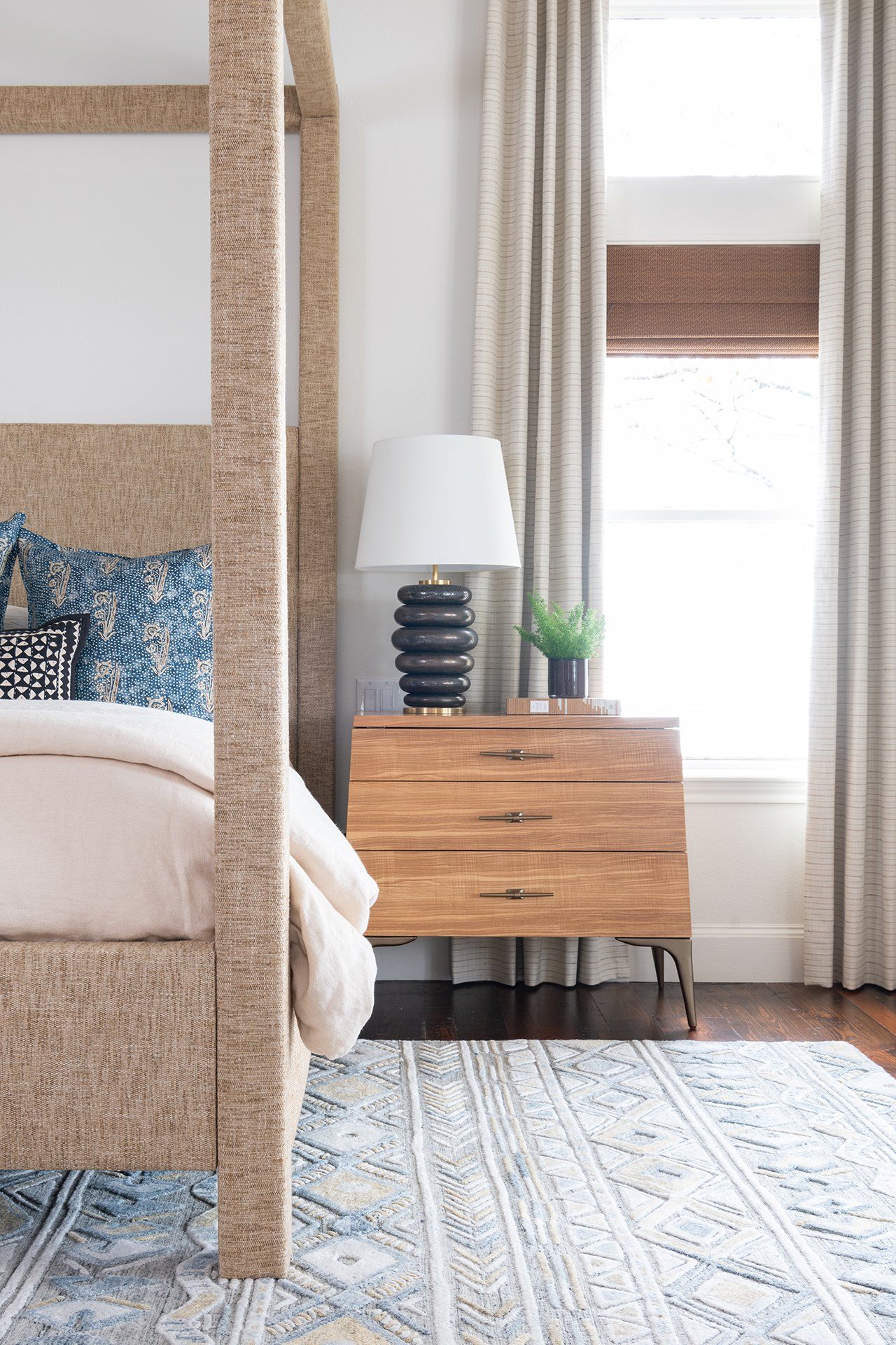 A bedroom with a canopy bed , nightstand , lamp and window.
