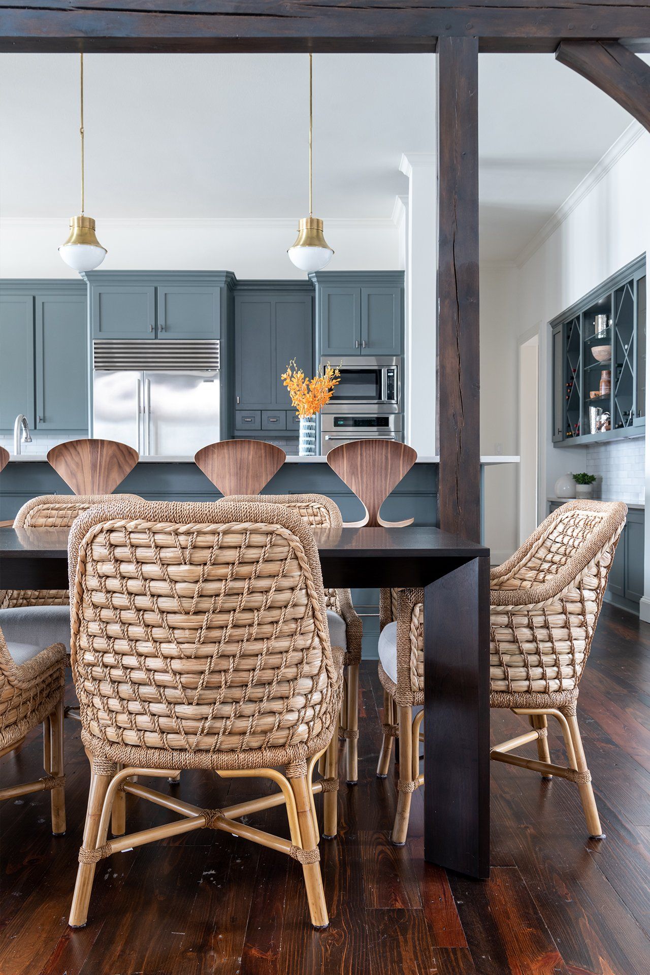 A dining room table with wicker chairs and a kitchen in the background.