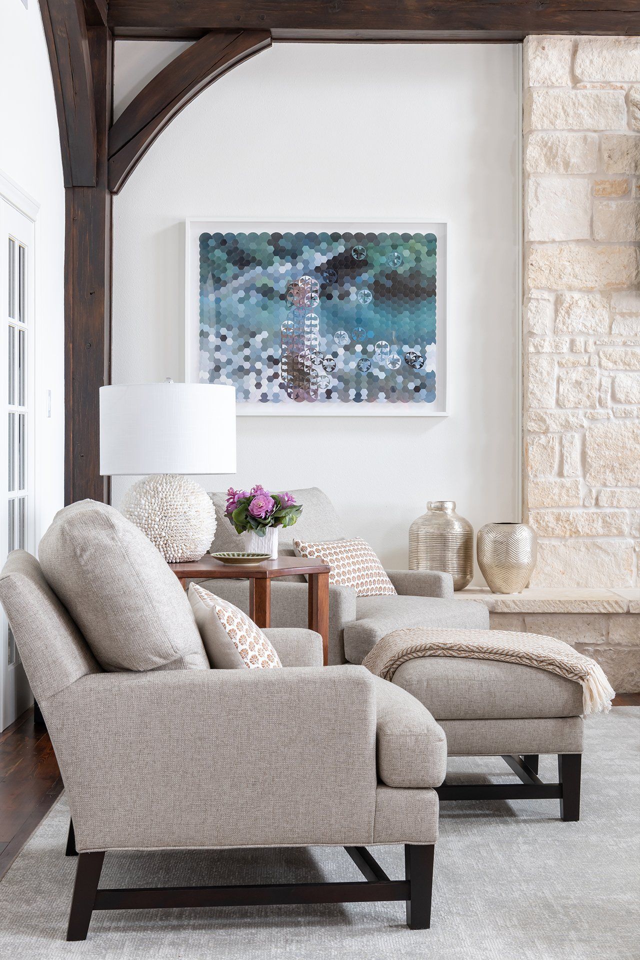 A living room with a fireplace , chairs , ottoman and a painting on the wall.