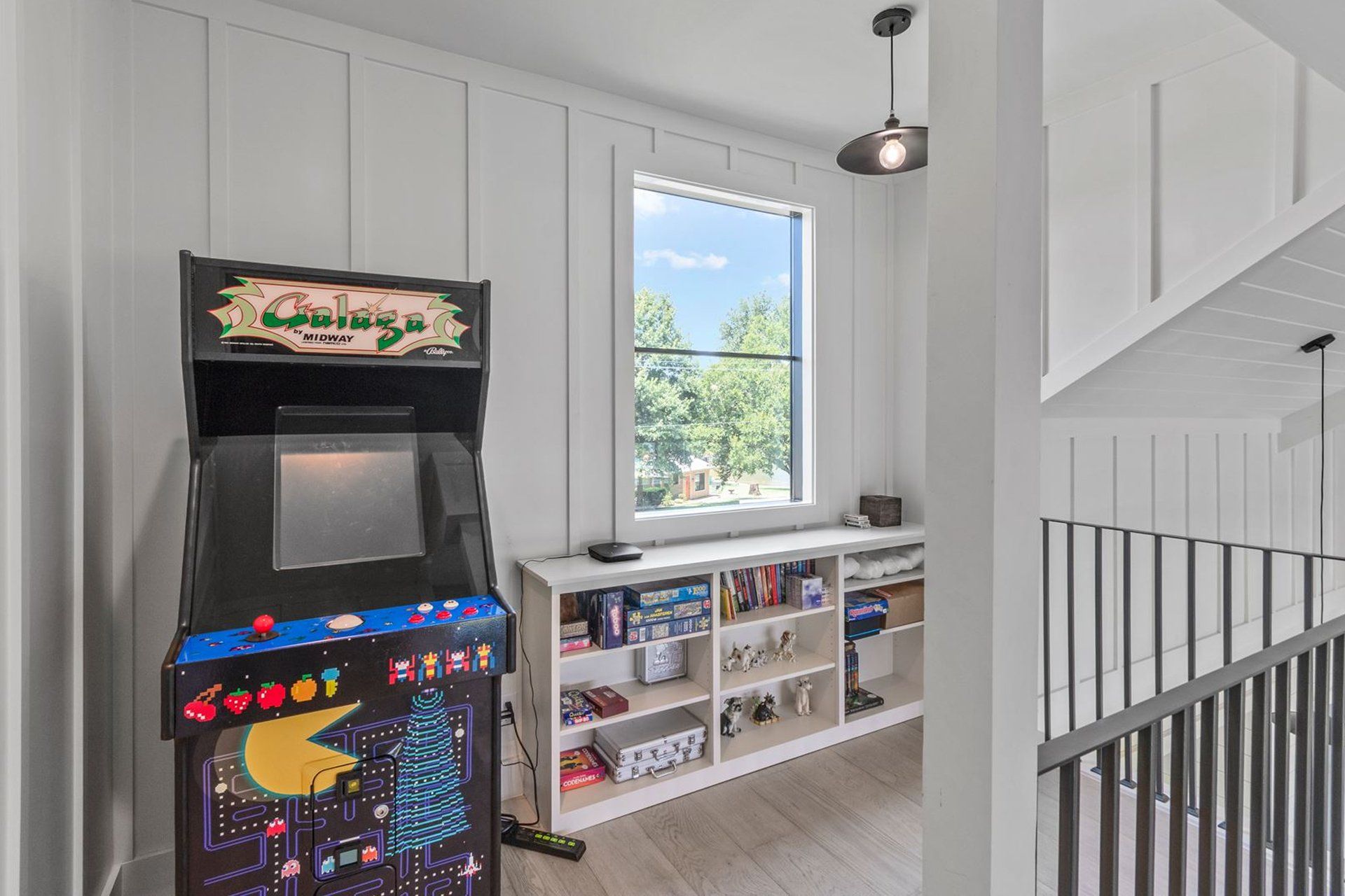 An arcade machine is sitting in a room next to a window.