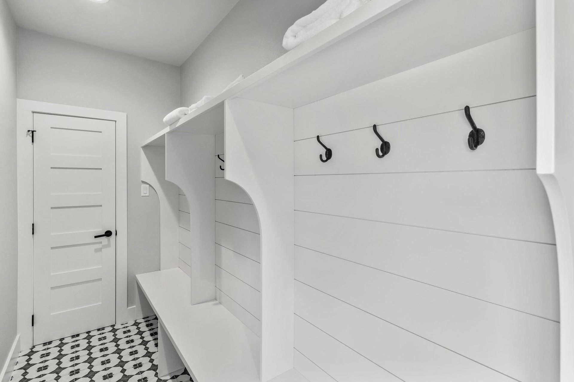 A black and white photo of a mud room with a bench and hooks.