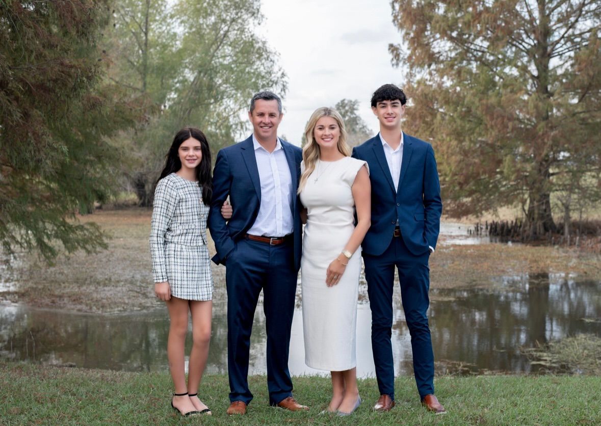 Family of Chasity Verret Martinez posing outdoors near water, wearing formal attire.