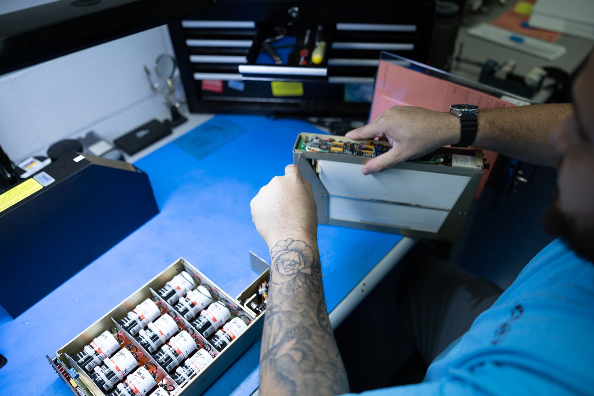 Person working with electronic components at a workbench, with tool cabinet in background.