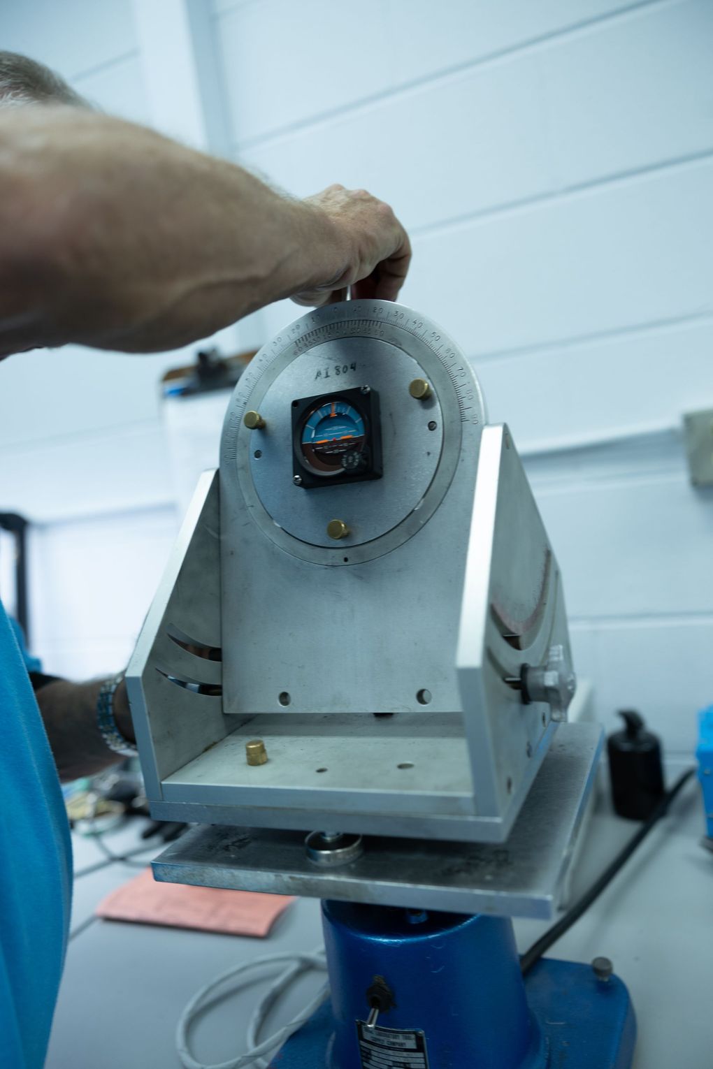 Person adjusting a metal instrument with a circular dial and mounted gauge, likely for calibration.