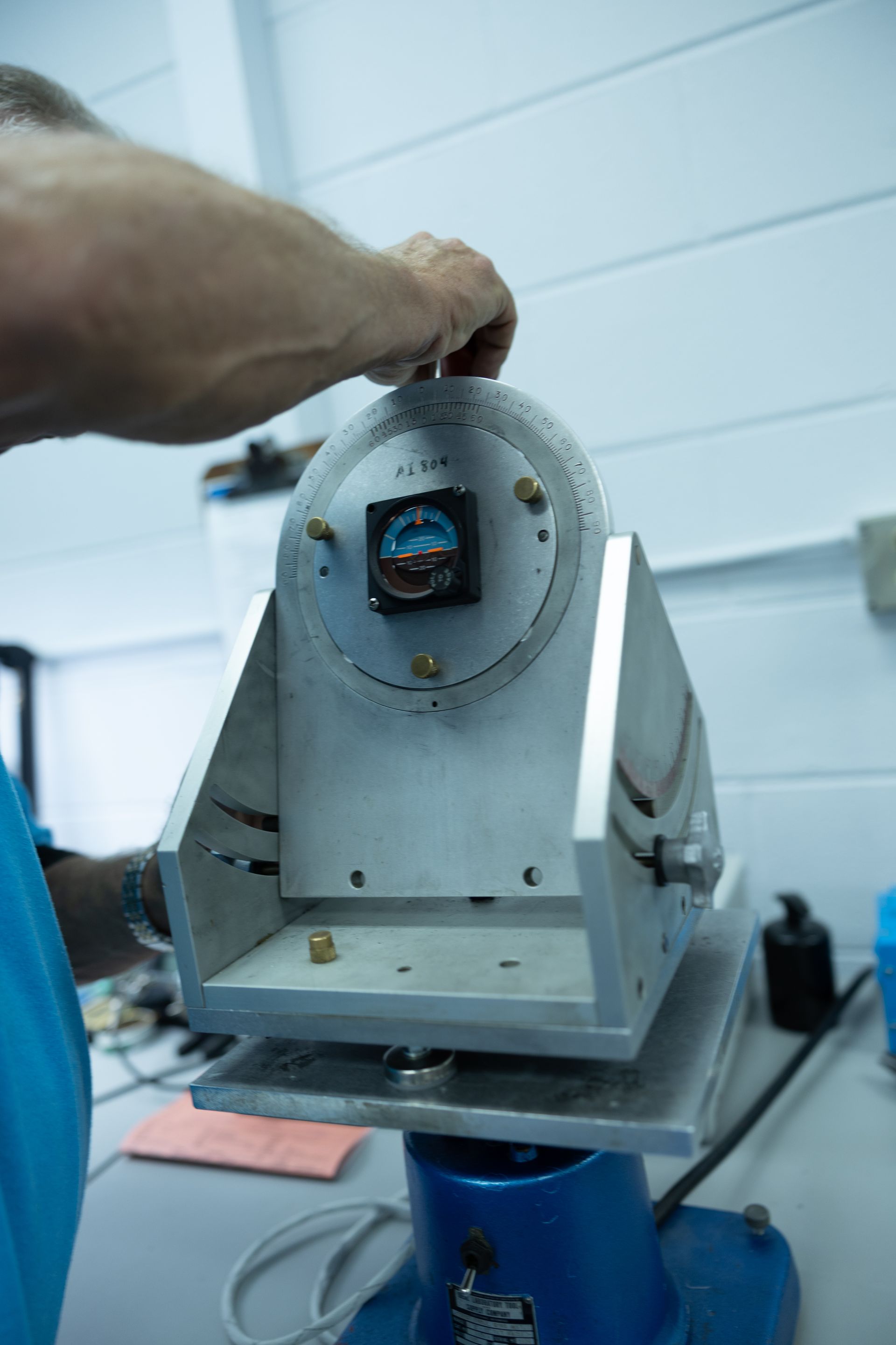 Person adjusting a metal instrument with a circular dial and mounted gauge, likely for calibration.