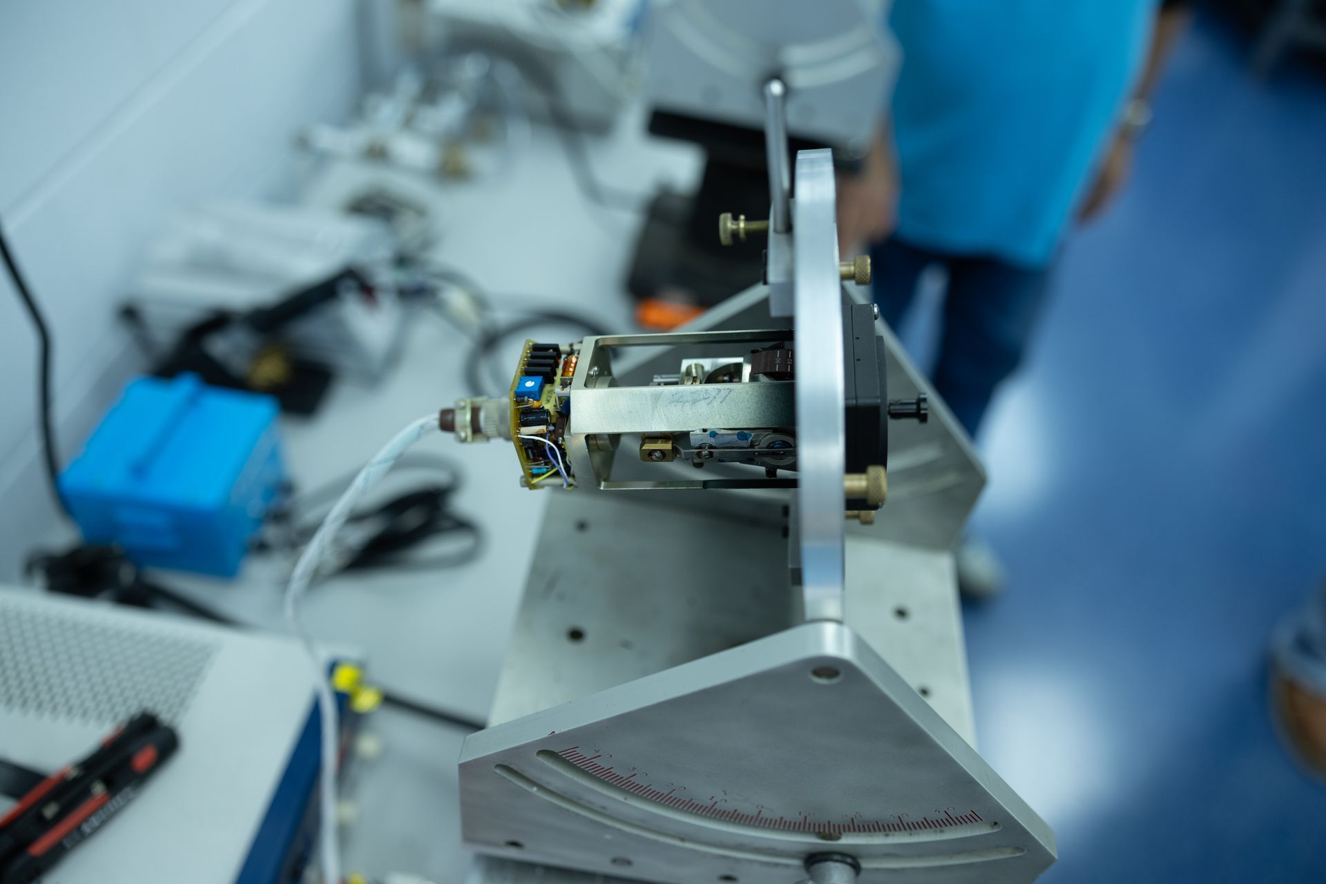 A circuit board mounted on an angled metal bracket. A person is partially visible in the background.