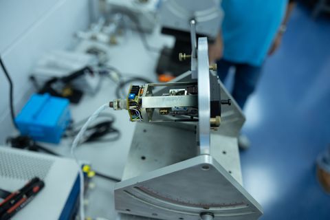 A circuit board mounted on an angled metal bracket. A person is partially visible in the background.