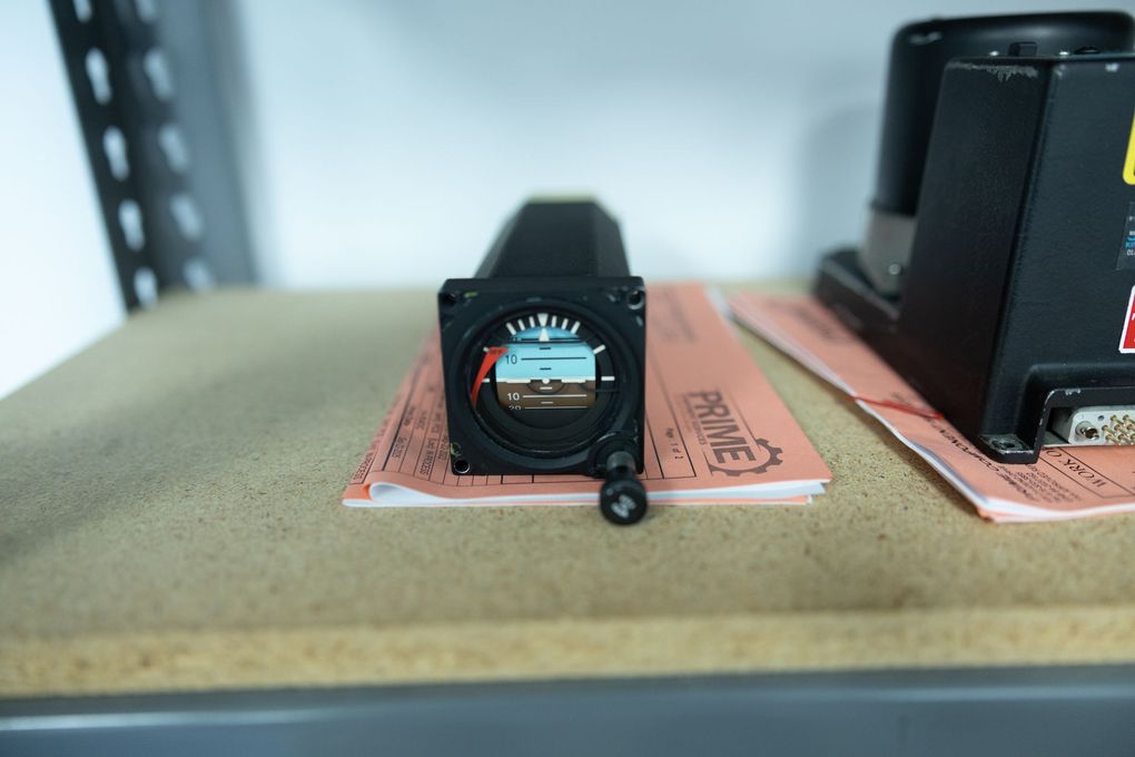 Avionics instrument (attitude indicator) on a shelf, showing an artificial horizon against a sky and brown background.