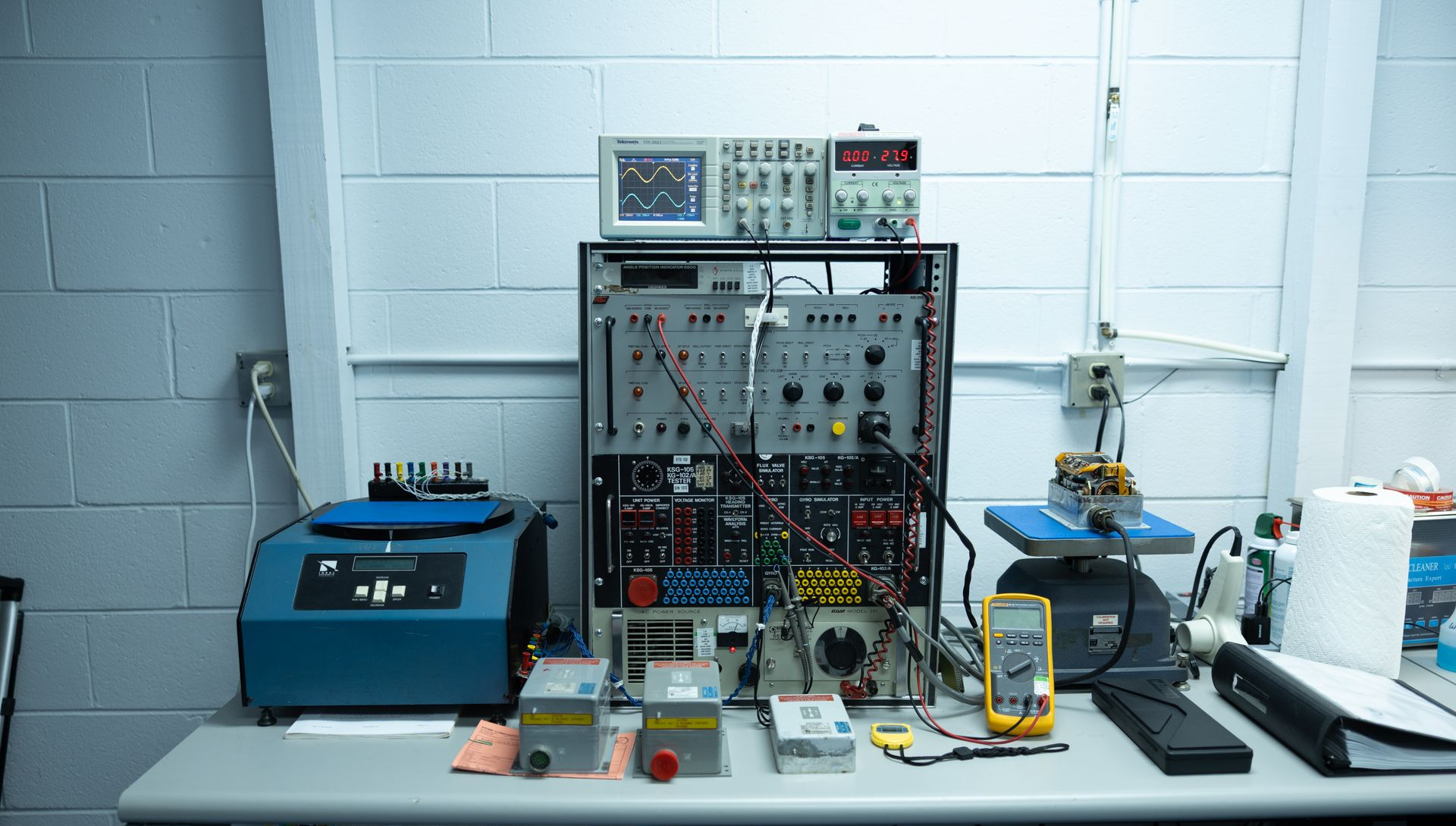 Laboratory workstation with electronic equipment on a white table against a white brick wall.