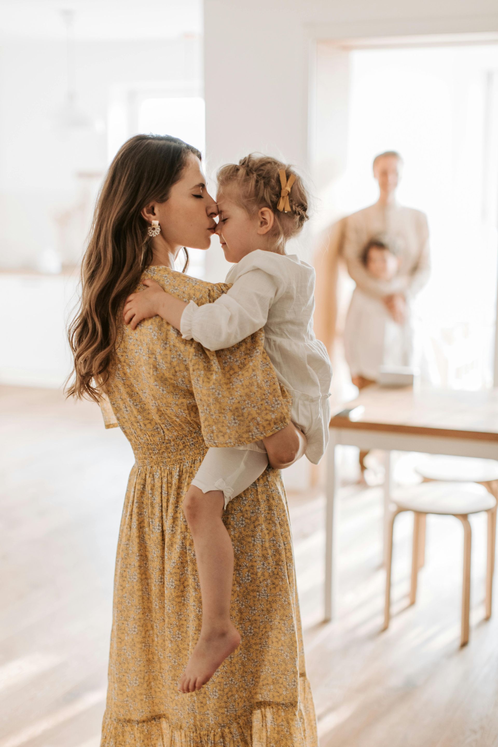 Woman in yellow dress kisses child; another couple in background.