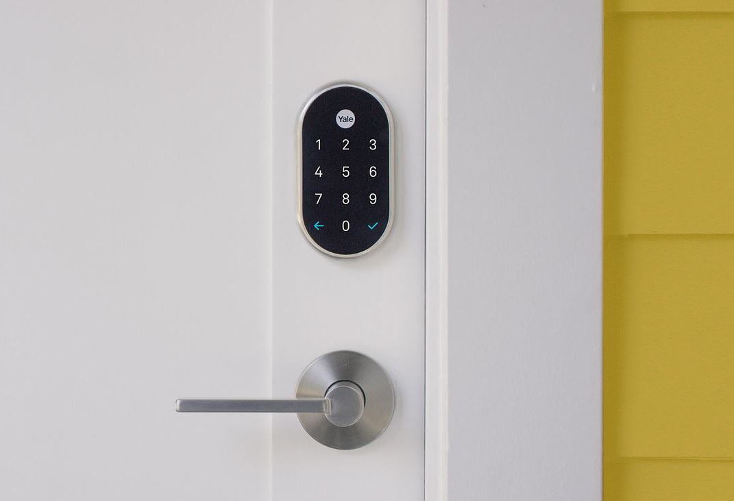 A Smart Door Lock is Sitting on a White Door Next to a Yellow Wall — SPL Security Solutions In Carrara, QLD
