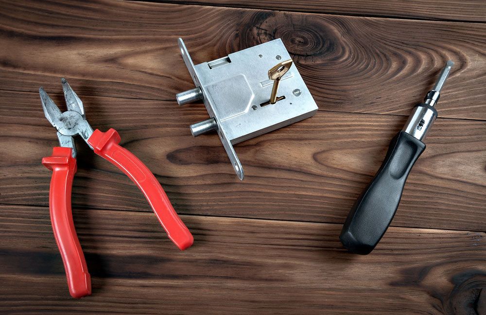 A Pair Of Pliers, Screwdriver, And A Lock On A Wooden Table — SPL Security Solutions In Runaway Bay, QLD