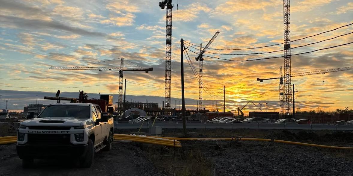 Camion garé sur un chantier avec des grues, sous un ciel de coucher de soleil.