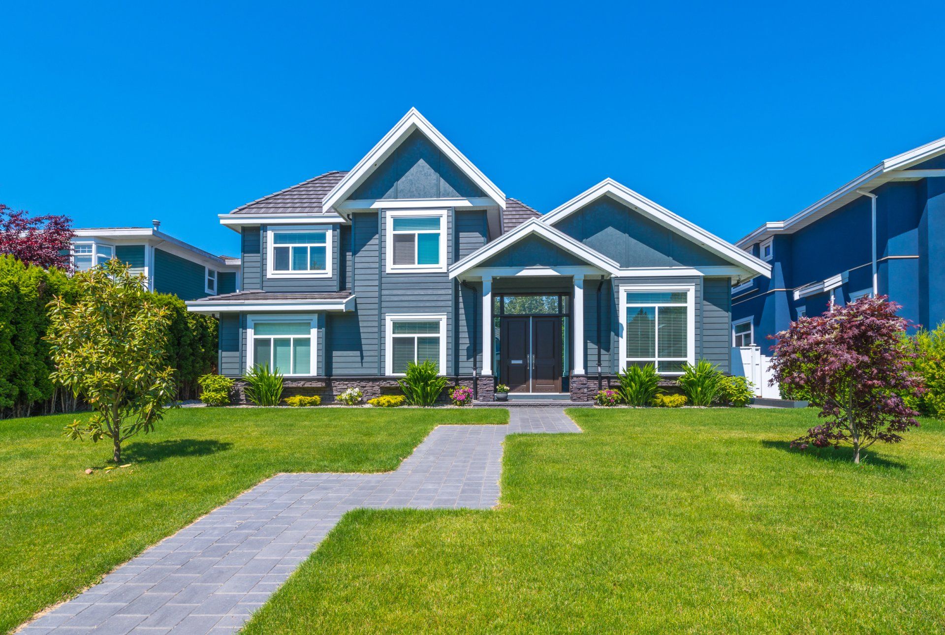 A large blue house with a lush green lawn and a walkway leading to it.
