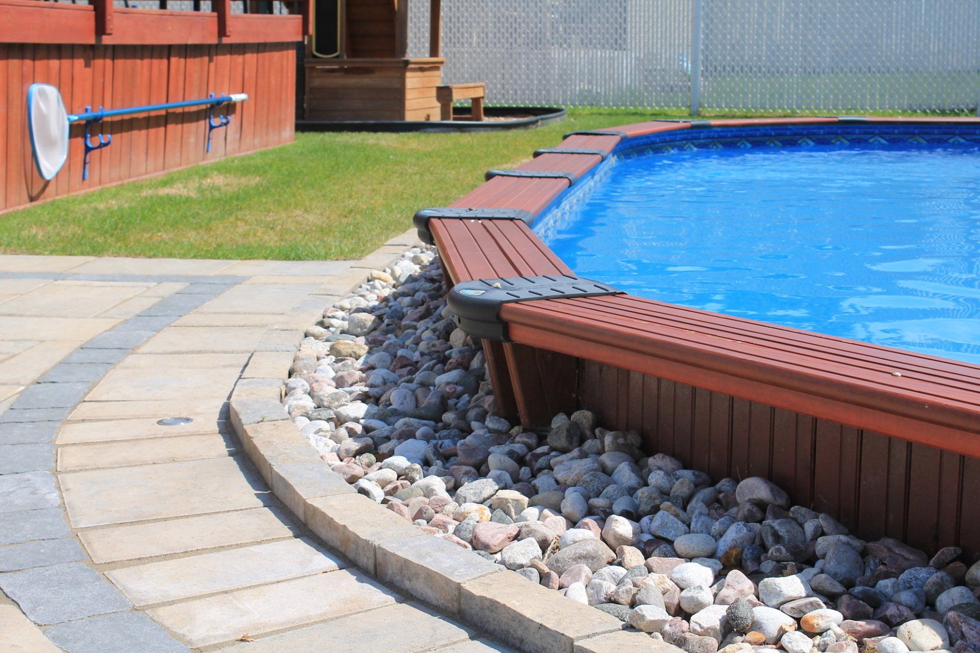 above ground pool with brown plastic siding surrounded by rock
