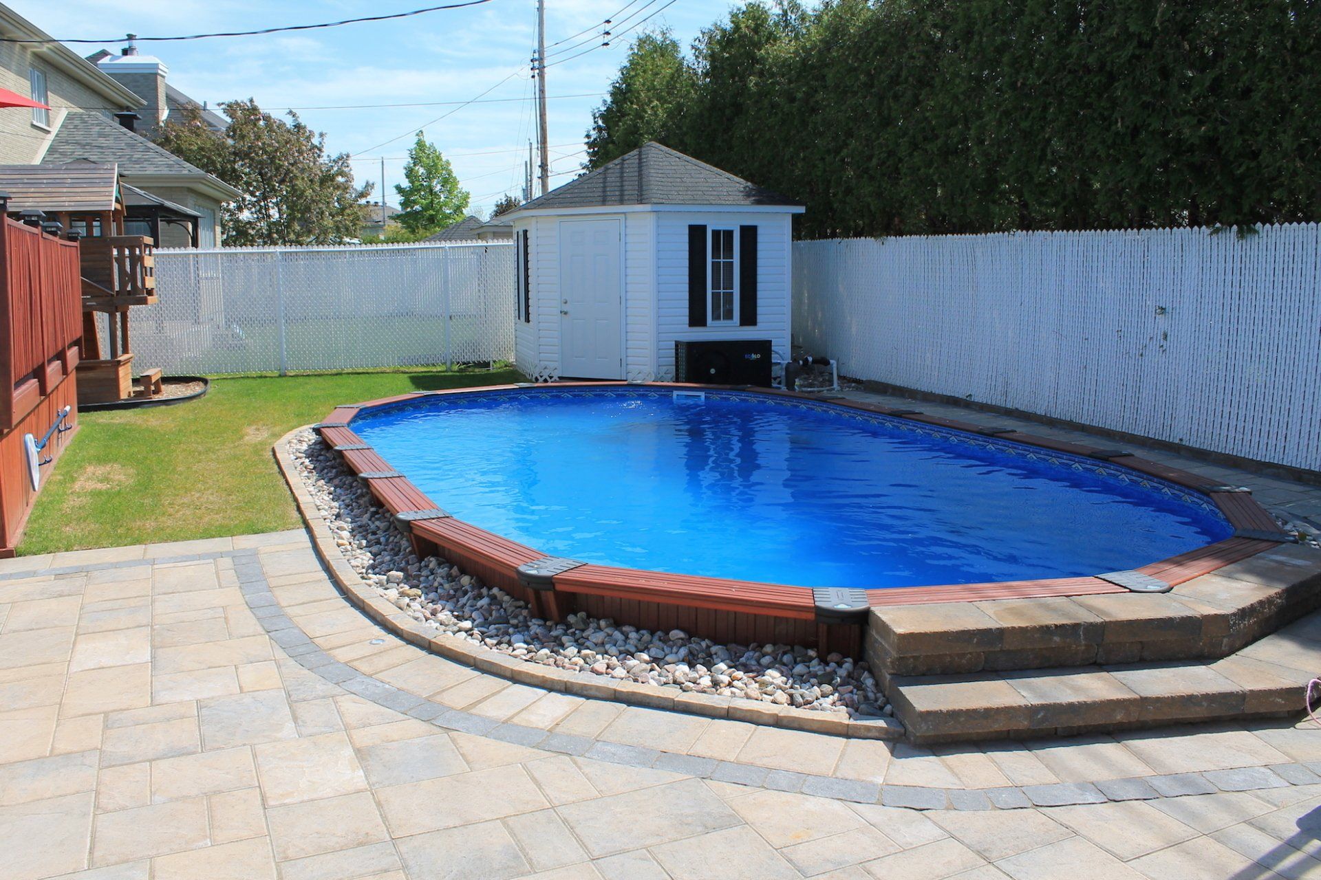 above ground pool surrounded by beige unistone and grass