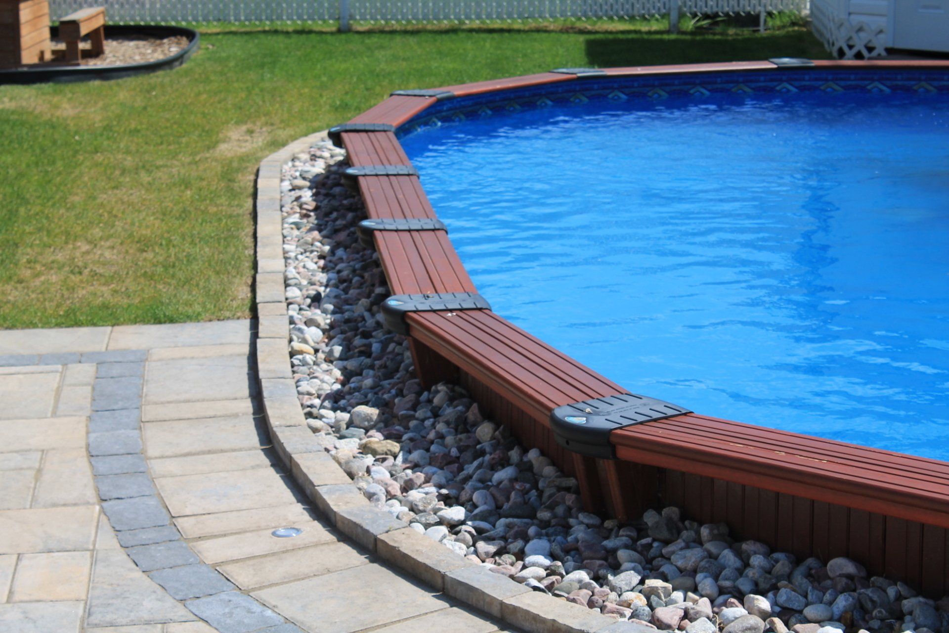 semi above ground pool surrounded by rocks and unistone