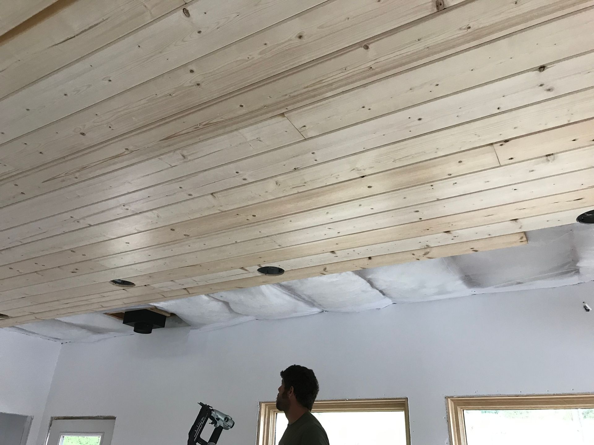 A man is working on a wooden ceiling in a room.
