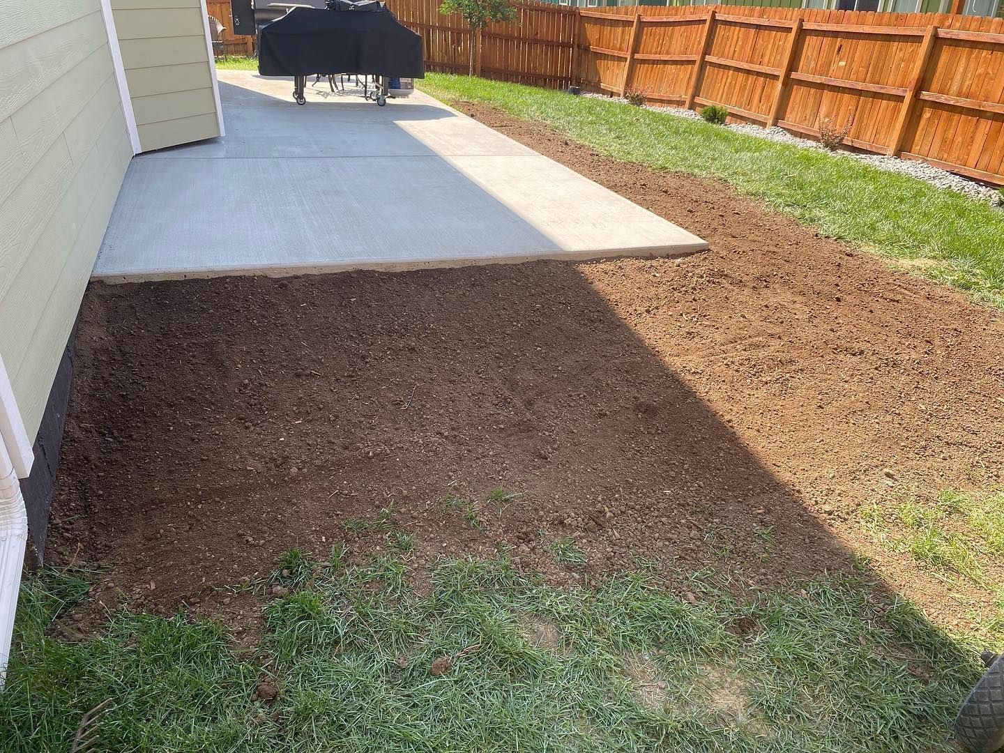 A patio with a grill and a wooden fence in the backyard.