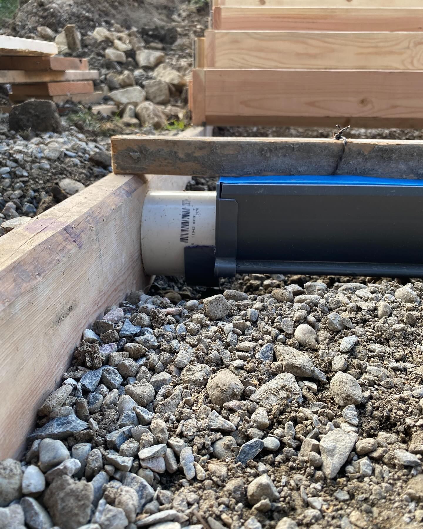 A pipe is sitting on top of a pile of rocks next to a wooden beam.