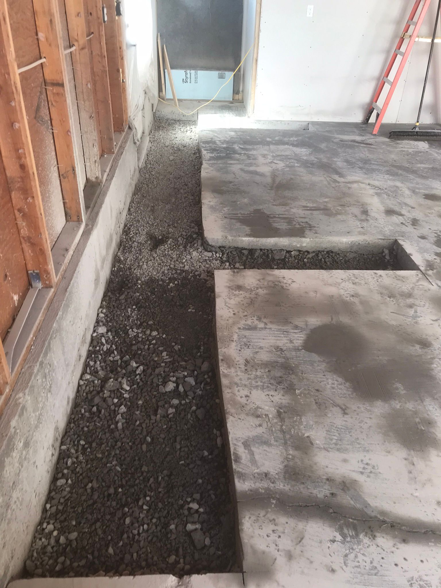 A concrete floor with a hole in it and a ladder in the background.