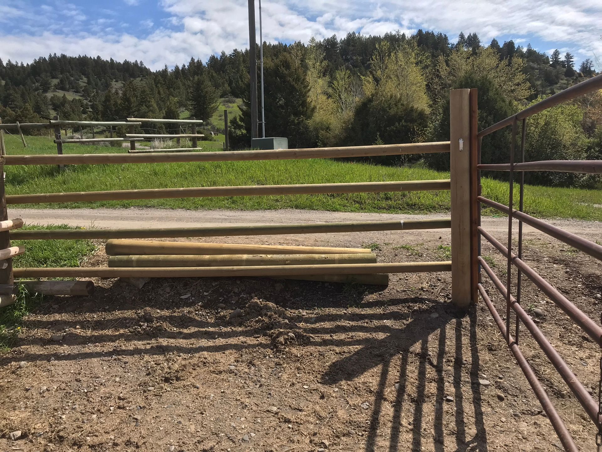 A wooden fence surrounds a dirt field with trees in the background