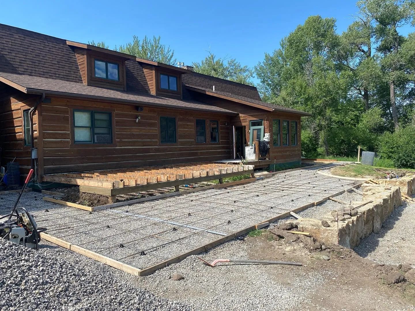 A log cabin with a gravel patio under construction; wood framing and building materials are present.