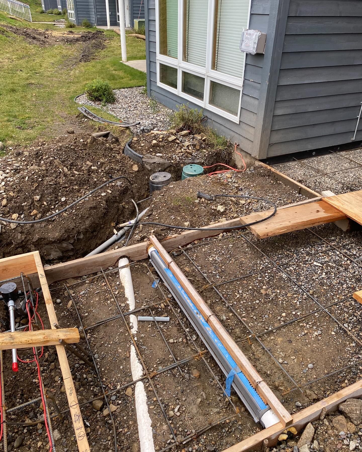 A house is being built in the backyard and a concrete slab is being poured in front of it.