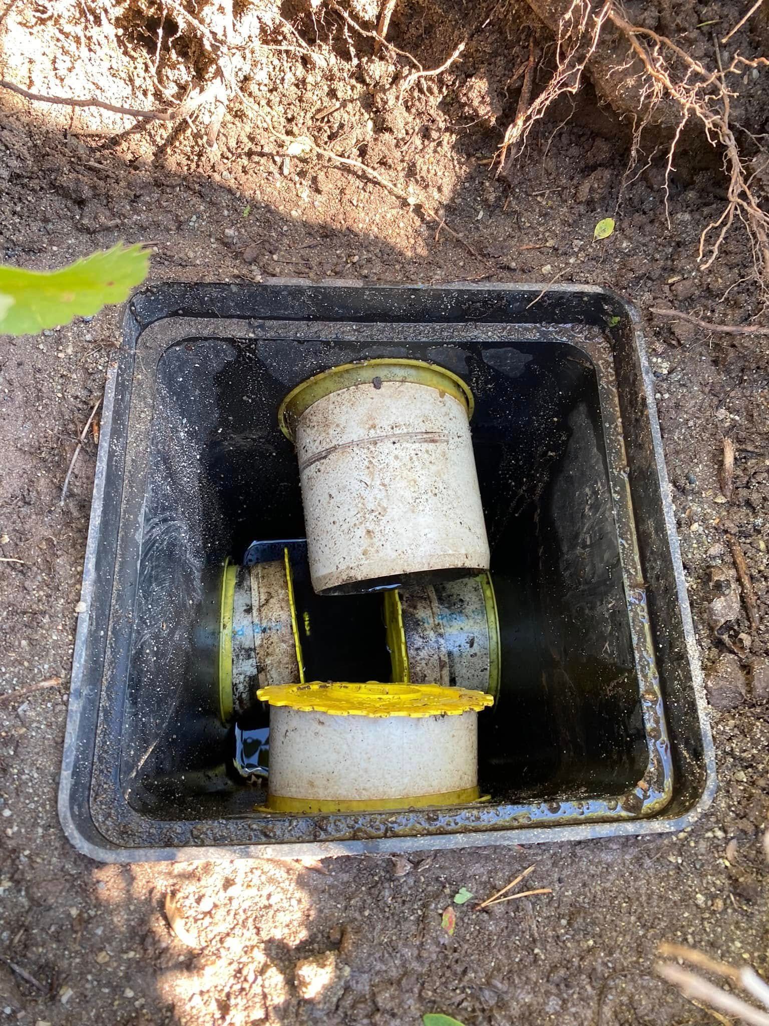 A close up of a drain box with a yellow pipe in it.
