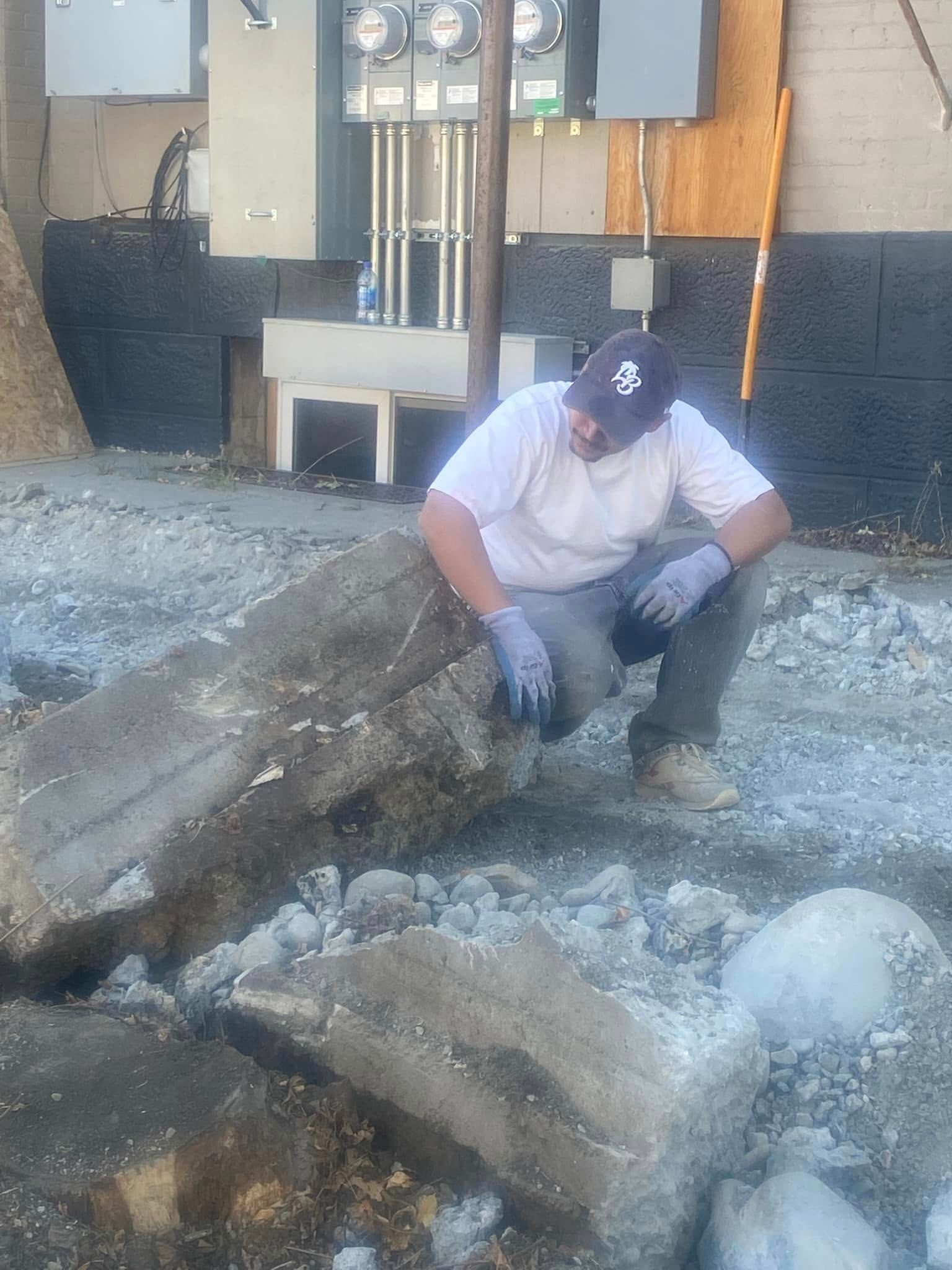 A man wearing a ny hat is kneeling on a pile of rocks.