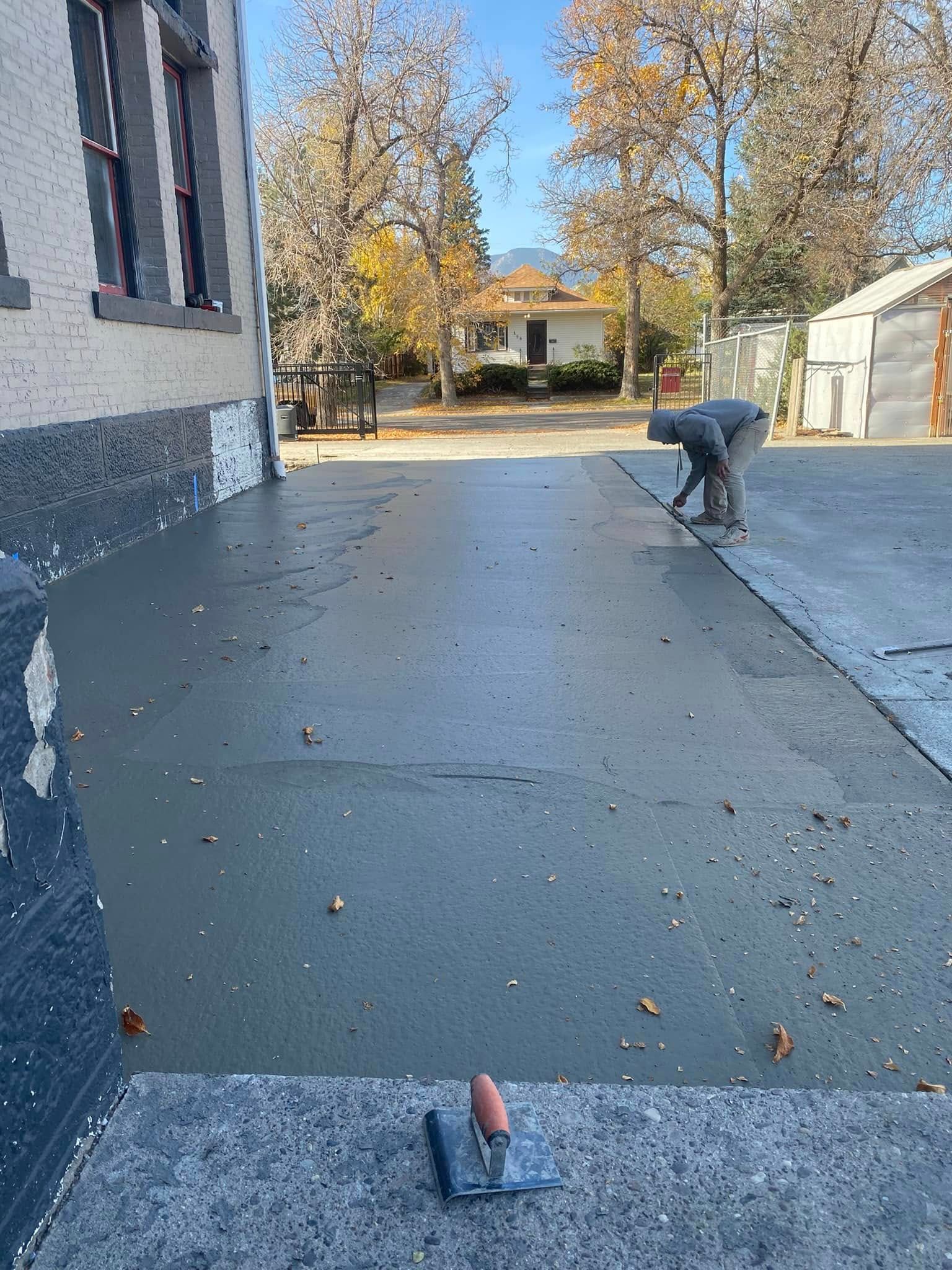 A man is working on a concrete driveway in front of a building.