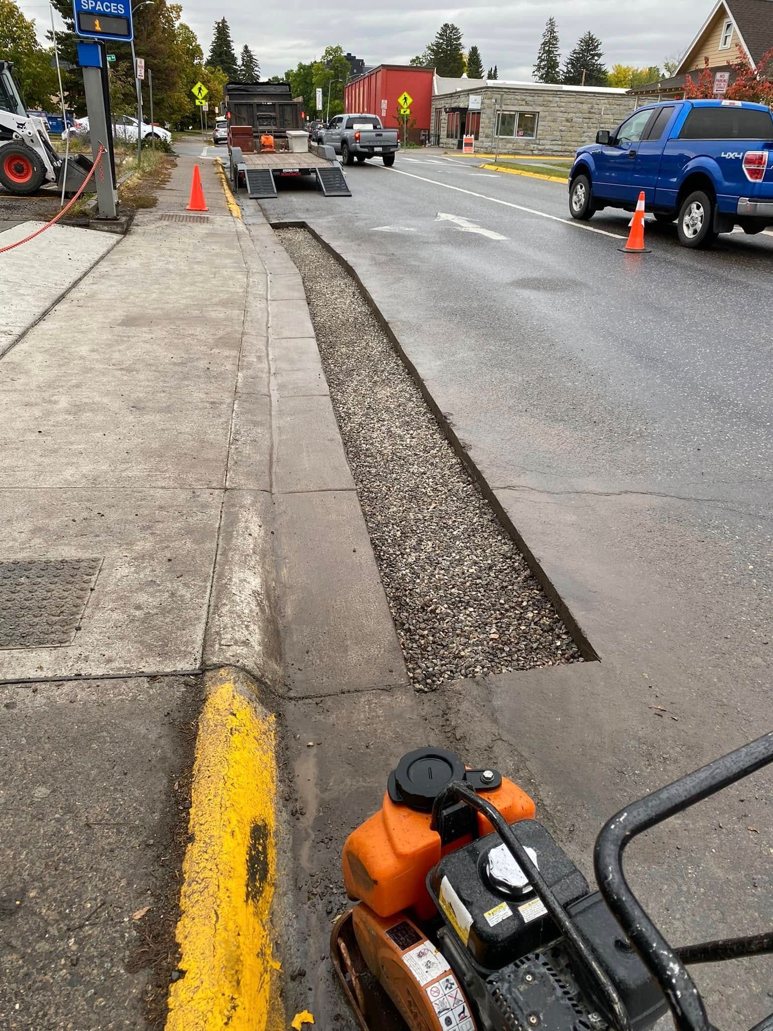 A blue truck is driving down a road next to a sidewalk.