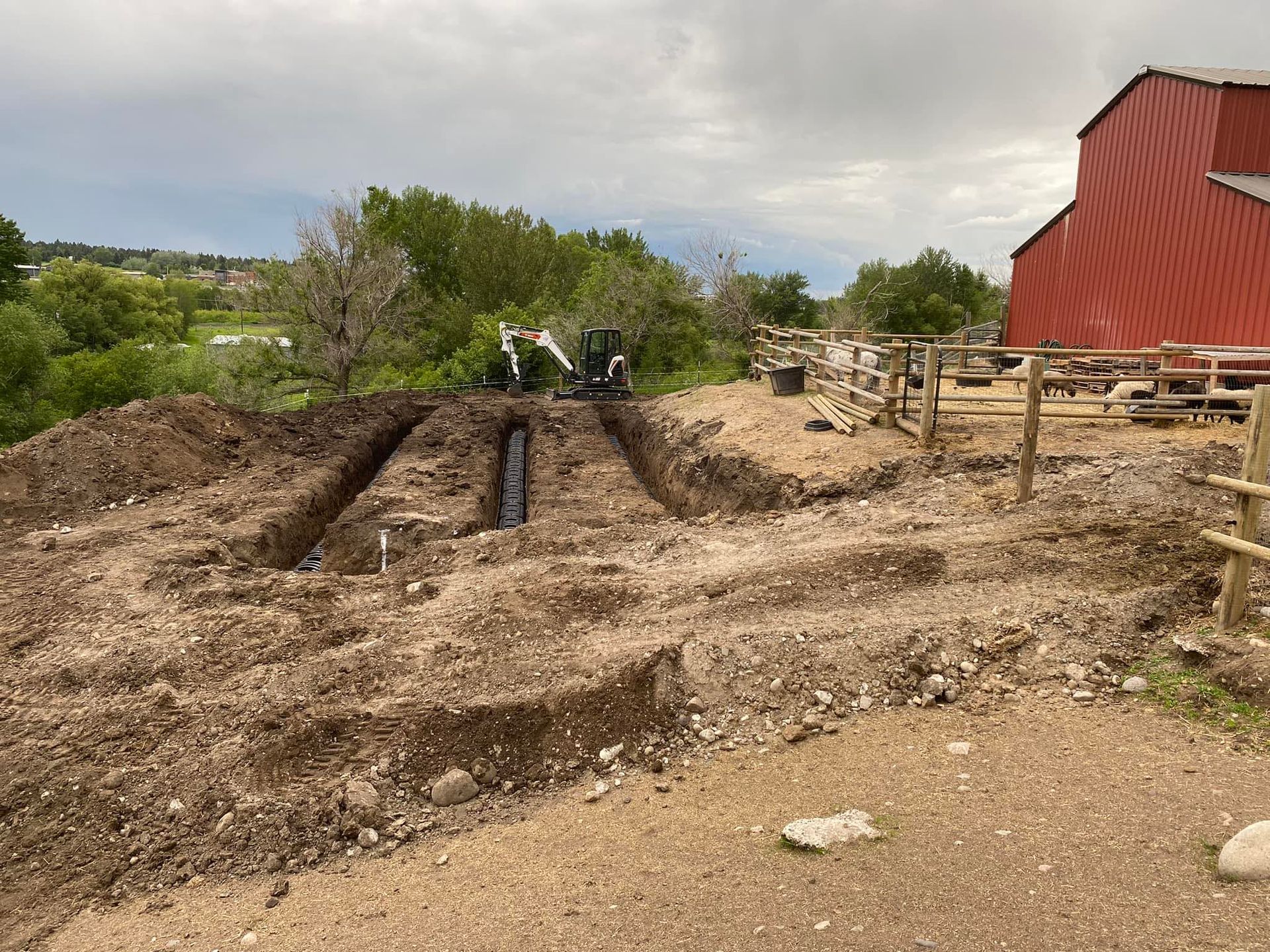 A large pile of dirt is sitting in front of a red barn.