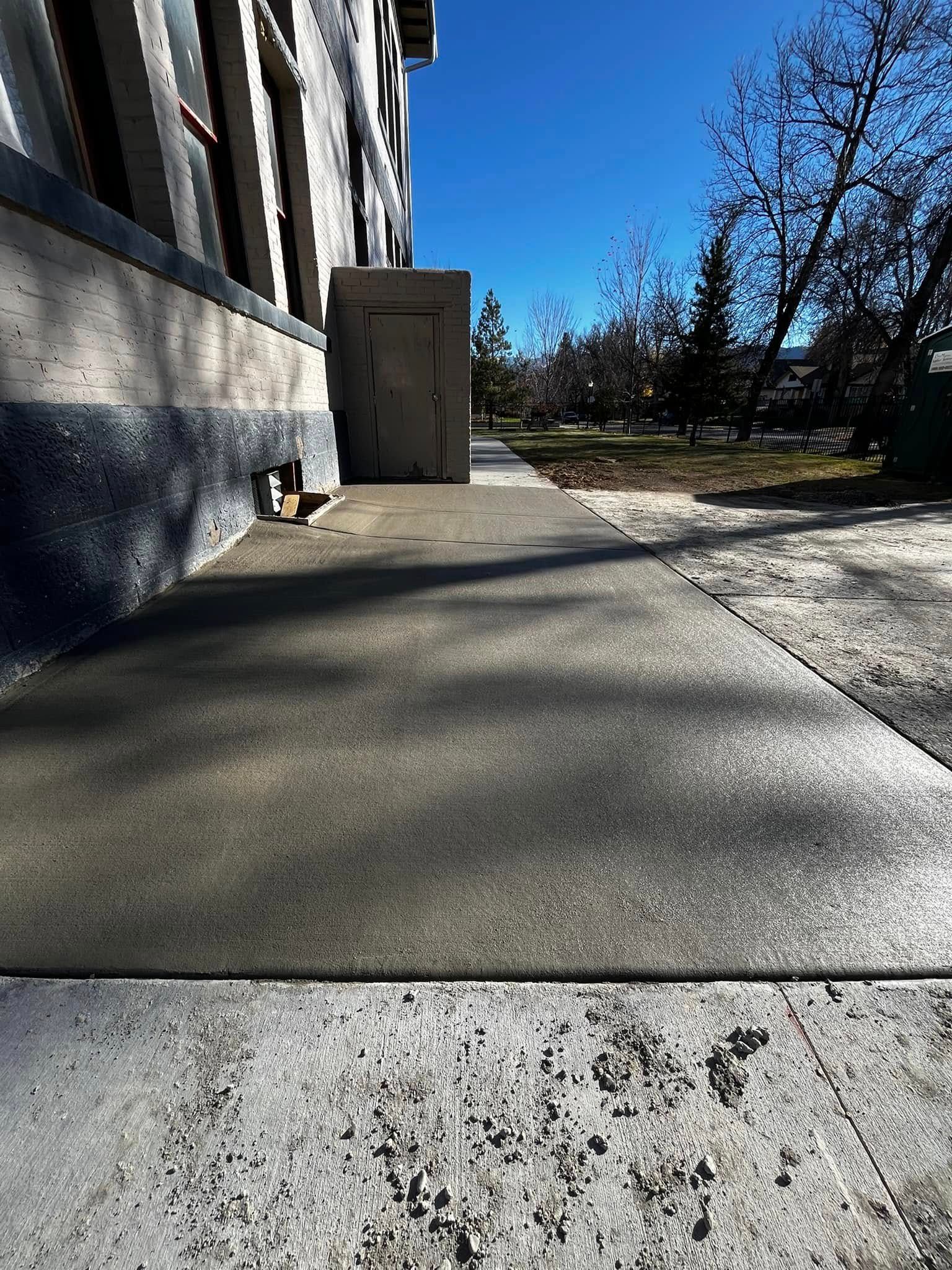 A concrete sidewalk next to a building with trees in the background.