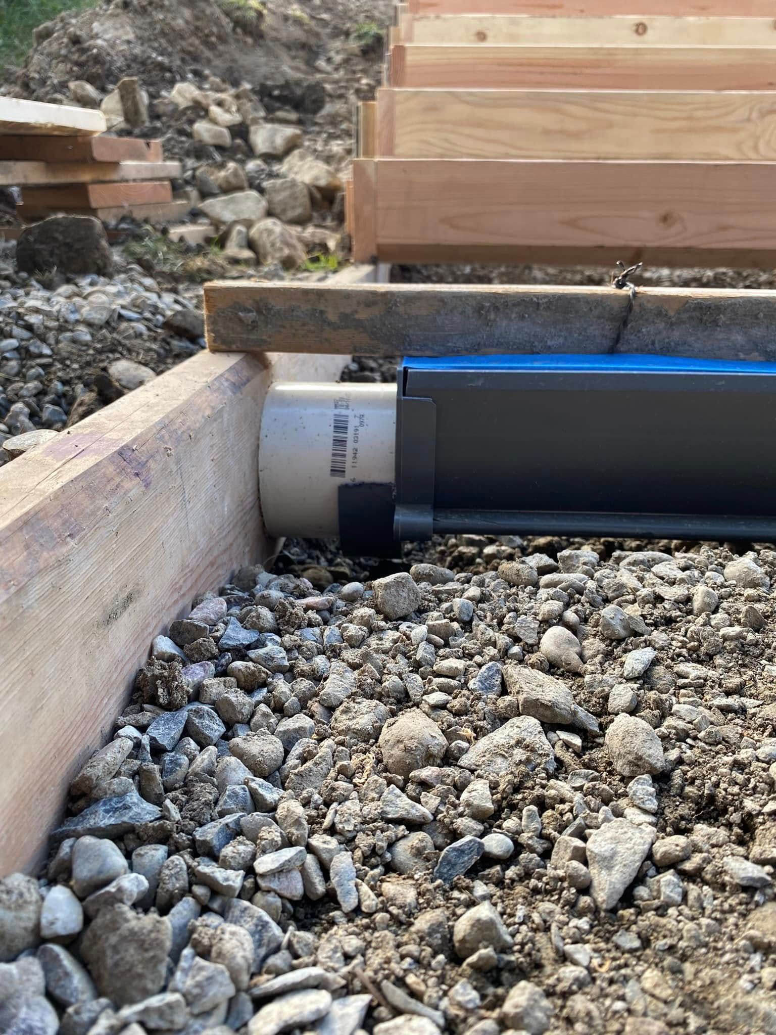 A pipe is sitting on top of a pile of gravel next to a wooden beam.