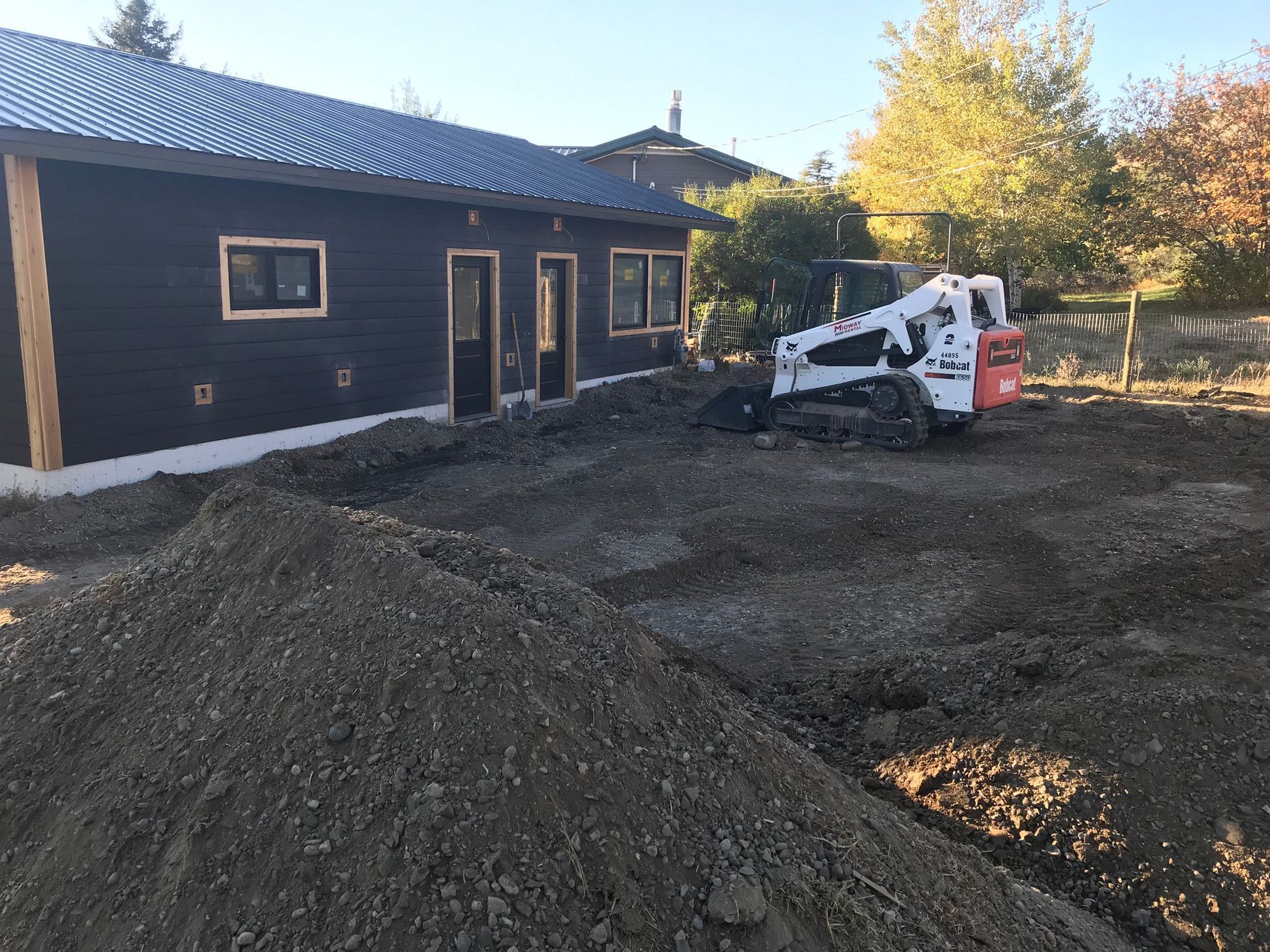 A bobcat is digging a hole in front of a house.