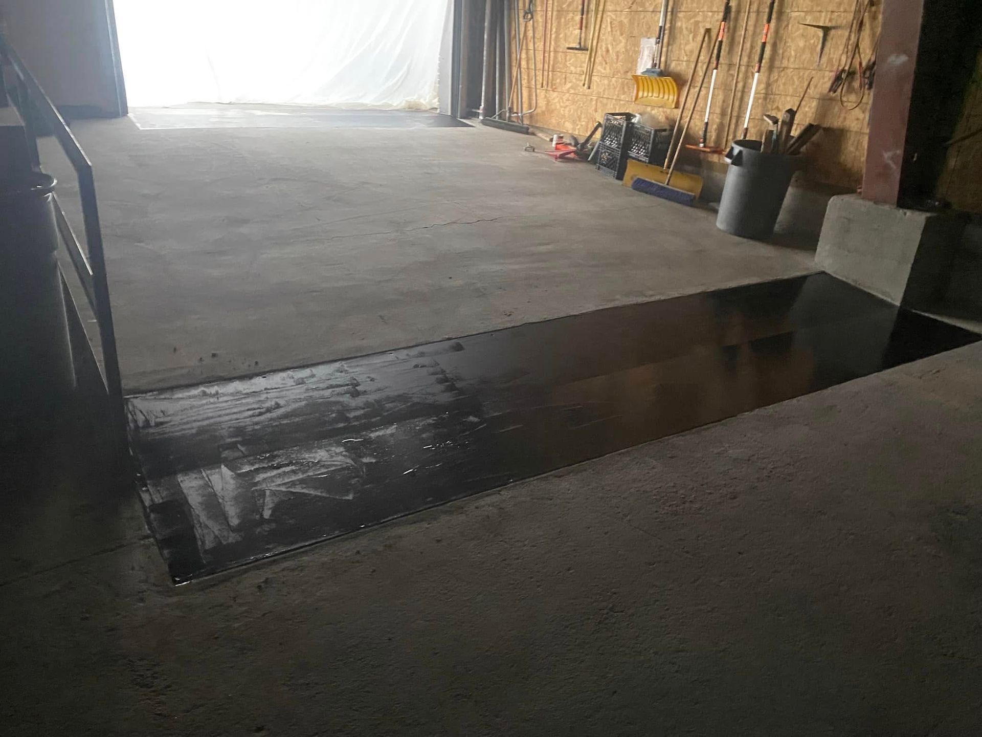 A garage with a staircase leading up to a door and a lot of tools on the wall.