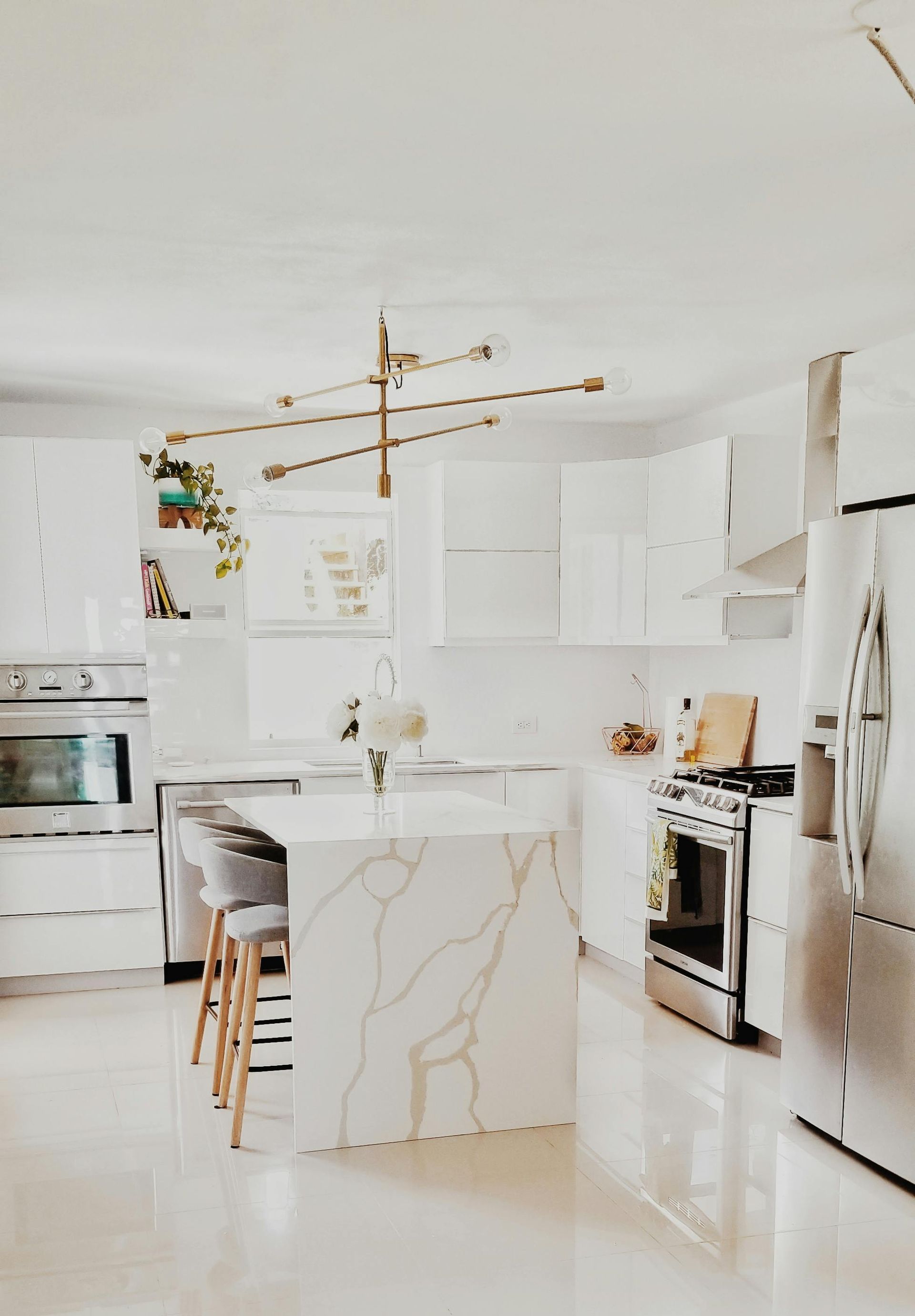 Bright, white modern kitchen with marble island, stainless steel appliances, and gold light fixture.