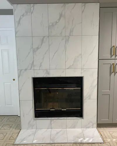 Fireplace with marble-look tile surround and black fireplace insert, set against a wall.