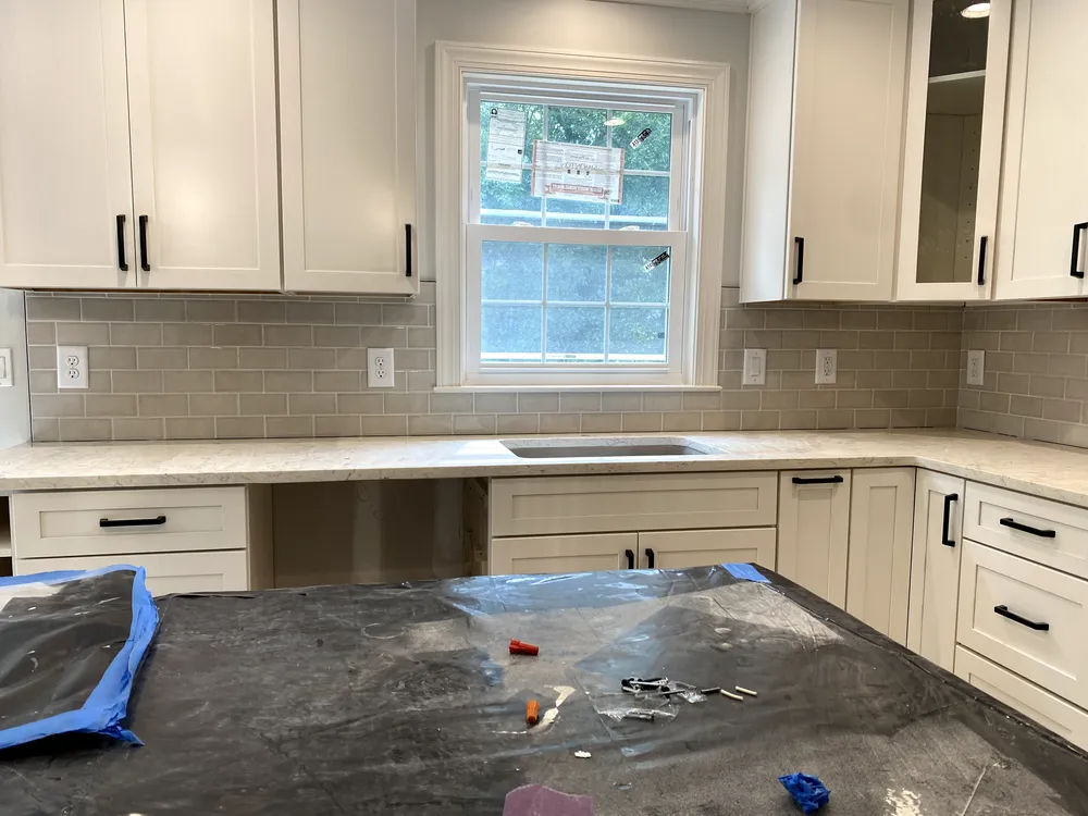 Kitchen with white cabinets, light gray tile backsplash, and dark countertop island.