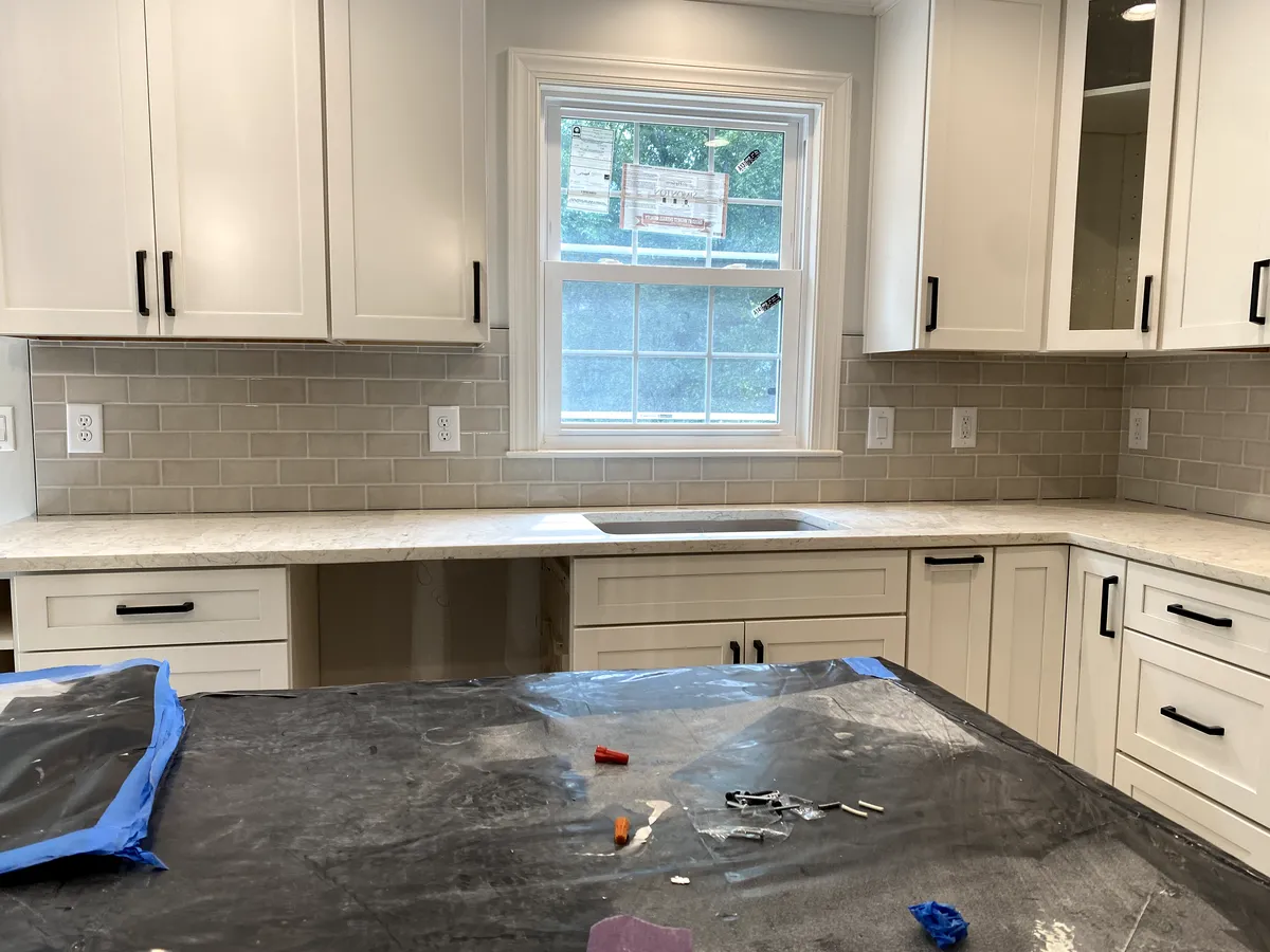 Kitchen with white cabinets, beige backsplash, and a black island.