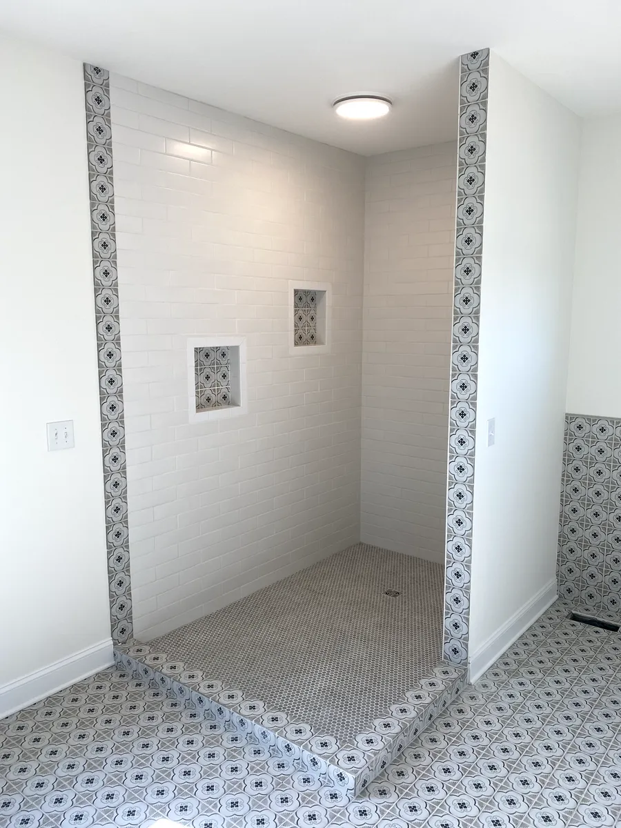 Tiled shower stall with white walls and a mosaic floor. Two inset shelves and a decorative tile border.