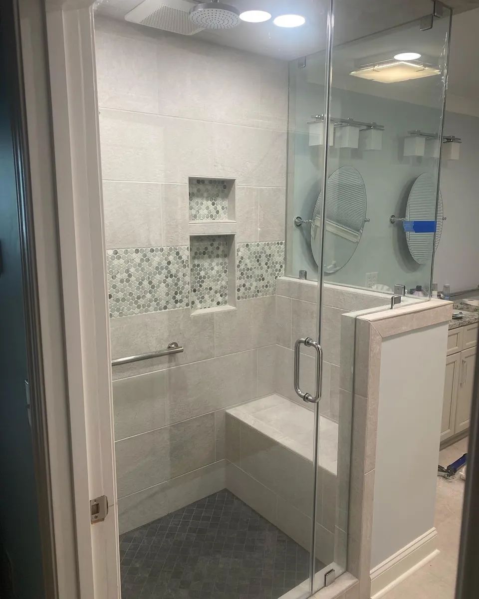 Glass-enclosed shower with a built-in seat, tiled walls, and grab bar.