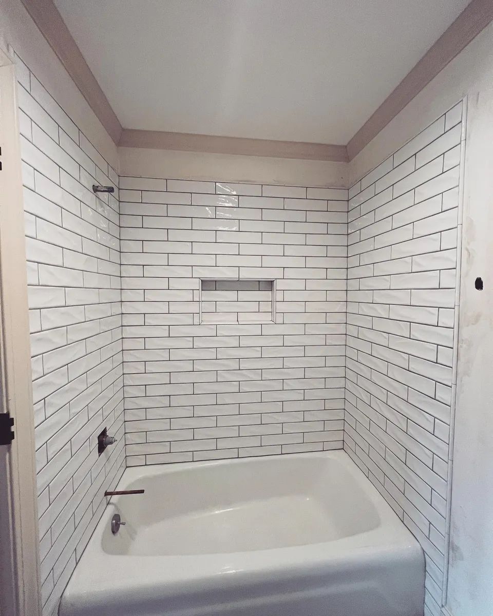 White tiled bathroom with a bathtub and a built-in shelf.