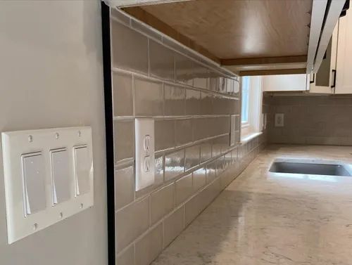 Kitchen with tiled backsplash, countertops, cabinets, and light switches on the wall.