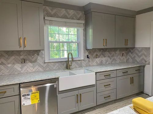 Grey kitchen with white countertop, subway tile backsplash, and stainless steel appliances.