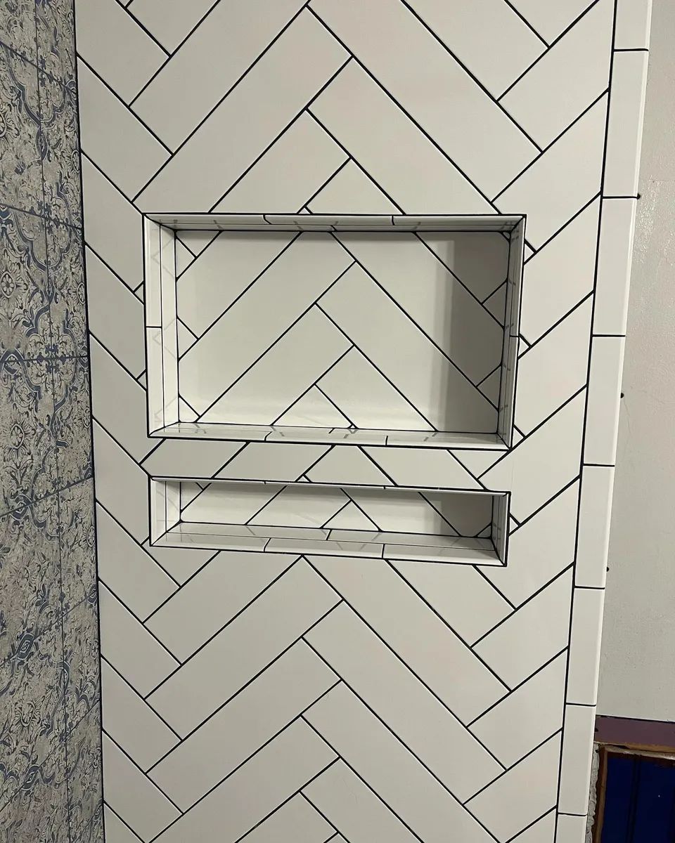 White herringbone tile wall with built-in rectangular shelving. Black grout lines.
