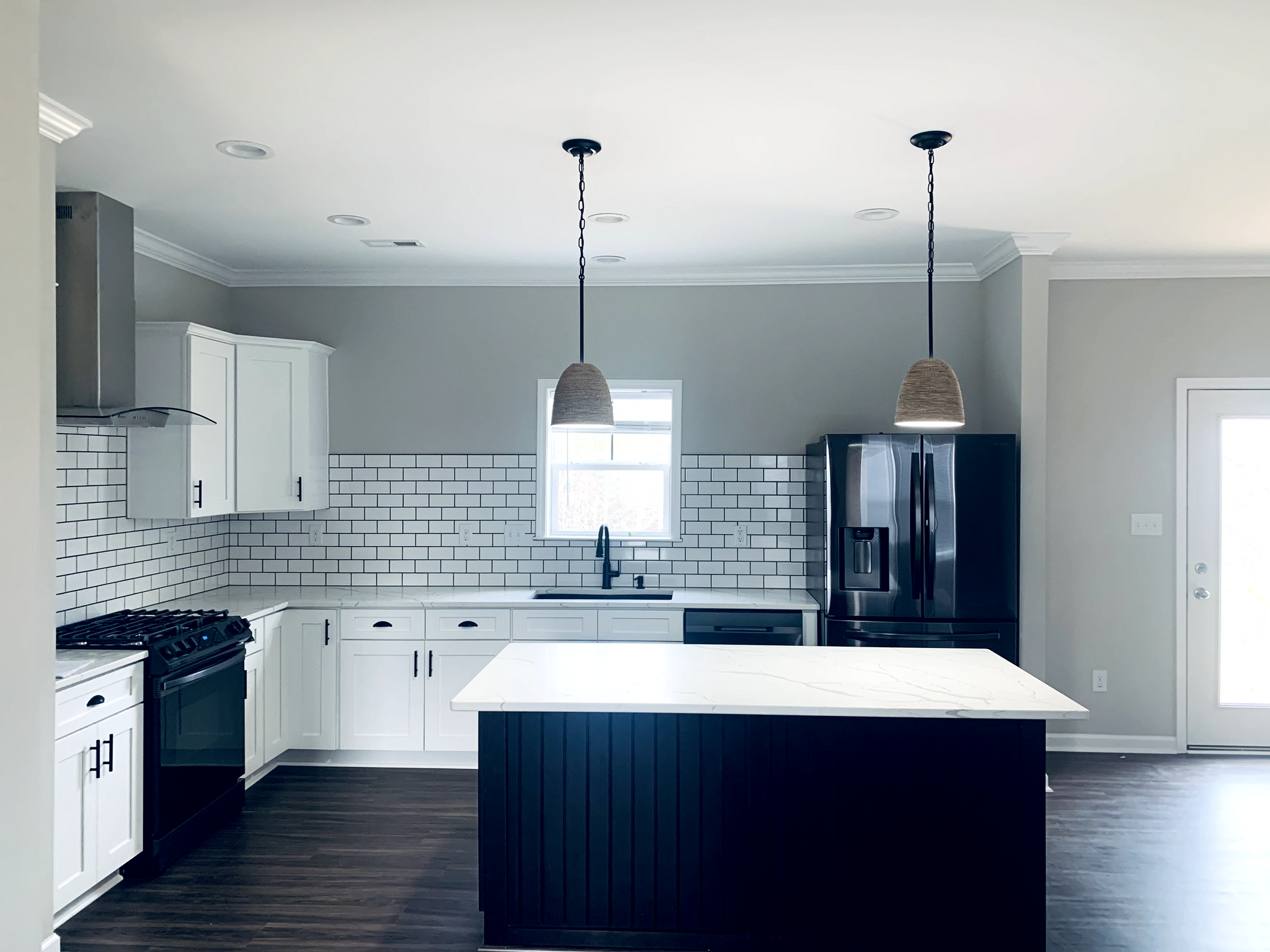 Modern kitchen with white cabinets, dark island, and exposed brick backsplash, featuring two pendant lights.